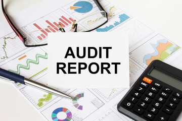 White card with text Audit Report it is lies on financial charts with a calculator and eyeglasses