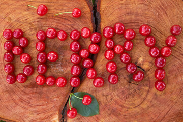 The word "berry" made from fresh ripe cherries on a cut wooden stump with a crack and tree rings texture. Berries laid out in the form of letters. Summer time. Particles of art.