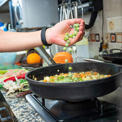 A hand pouring peas over sautéed vegetables in the pan. Healthy food concept.