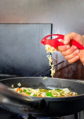 Close-up of Woman's hands crushing a garlic with a kitchen utensil and pouring it directly over the stew in the pan. Healthy food concept.