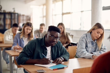 African American student writing notes while attending class in lecture hall.