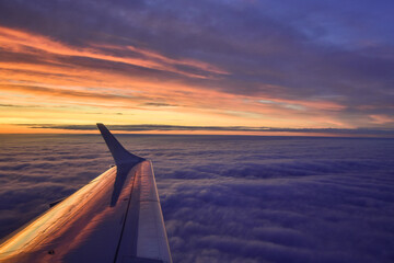 Airplane wing flying above the clouds in front of a colorful sunset