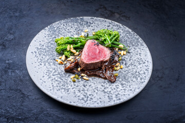 Modern style barbecue dry aged angus beef filet steak natural with broccolini and cep mushroom served as close-up on a design plate with copy space