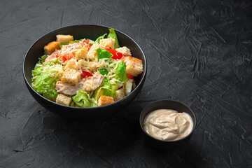 Caesar salad in a black ceramic plate with sauce on a black background.