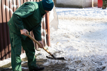 The landlord of the district in a housing estate in the city scrapes the snow off the pavement with a metal shovel