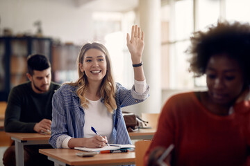 Happy female student raising arm to ask question in the classroom.