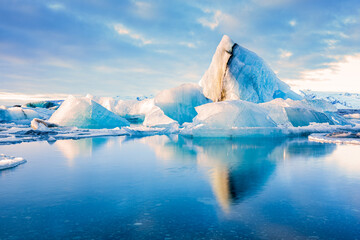 Icebergs float on Jokulsarlon glacier lagoon with mountain peaks lit by the warm sunrise light, in Iceland. © mandritoiu