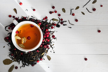 Tea leaves with lingonberry berries and a cup of tea on a white background with space for text. The...