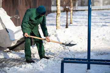 A manual worker scoops snow from the pavement and shovels it onto a pile next to it
