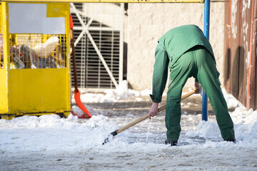 A manual worker scoops wet snow and ice on a shovel