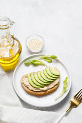 Bran bread toast with chickpea hummus and avocado on white stone table background. Flat lay, top view, copy space