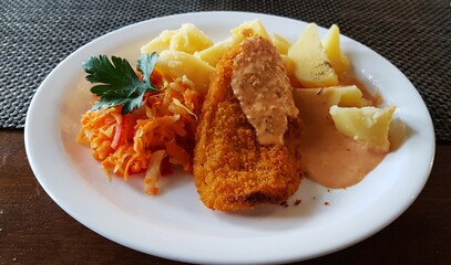 Piece of fish in bread crumbs with boiled potatoes on a ceramic plate
