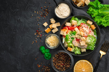 Delicious Caesar salad with ingredients, lemon and spices on a black background.