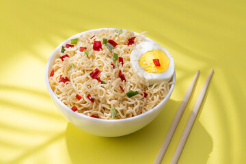 Instant noodles with vegetables and herbs in bowl on yellow background