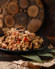 hot second courses of Japanese cuisine. Chahan rice with white sesame seeds, mussels and vegetables in a black bowl on a slate board with bamboo leaves on a brown background