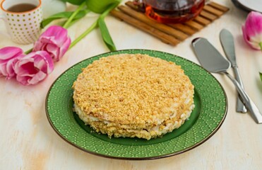Whole traditional chopped dough Napoleon cake with custard on a green plate on a light concrete...
