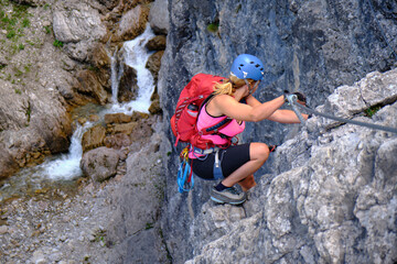 Woman tourist climbs Hanauer via ferrata route in Tirol, Austria, near a water stream. Adventure, tourism.