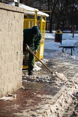 A manual worker scrapes snow off the pavement with a metal shovel