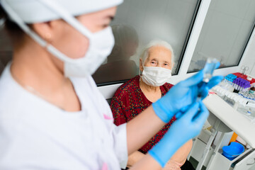a nurse wearing a mask and rubber gloves is preparing to vaccinate an elderly woman against viral diseases. Prevention of coronavirus infection