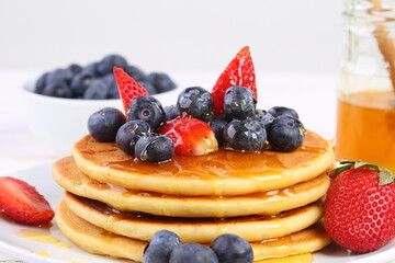 Still life with pancakes, berries and honey on a white background