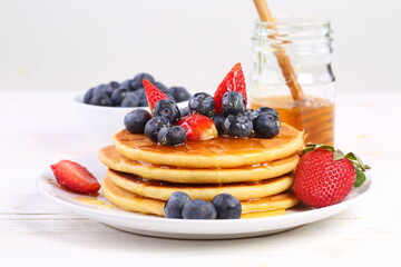 Still life with pancakes, berries and honey on a white background