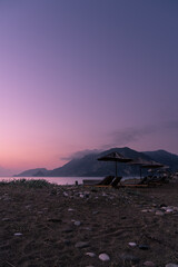 A beach in south Turkey with sunbeds and sunshades at dawn with a hazy atmosphere, mountain ranges and clouds in the background