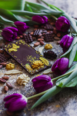 Obraz na płótnie Canvas Assortment of different chocolate types in cocoa beans, with violet spring tulips on the background