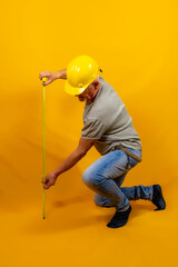 craftsman worker with hard hat is measuring with a tape measure isolated on yellow background