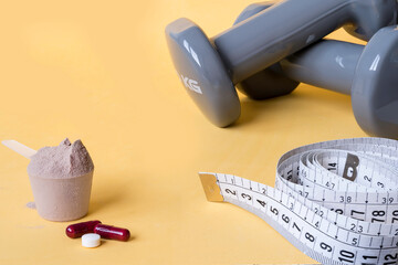 Weights and a tape measure along with pills and dietary supplements on yellow background. Sport supplements. Healthy diet concept