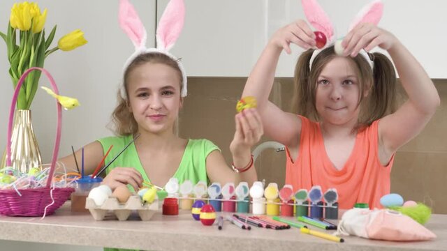 Two cute girls play and show the camera decorated Easter eggs. Easter holiday. Rabbit ears on the head.