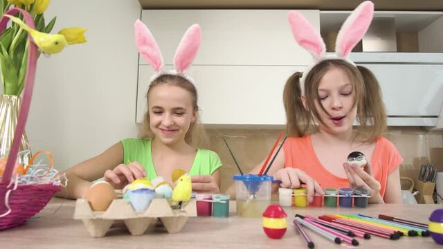 Two sisters together decorate Easter eggs with colors, talk and laugh. Easter holiday. The camera moves from right to left. 4k video.