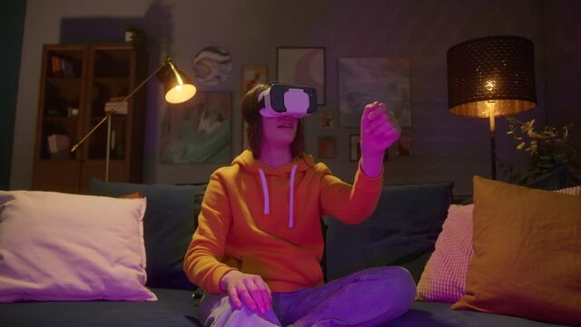 Young woman in VR headset looks around and wonders how amazing. Virtual reality helmet, enjoying the proccess, neon light