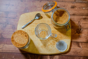 A cup of tea on a wooden chopping board with a brown sugar bowl next to it.