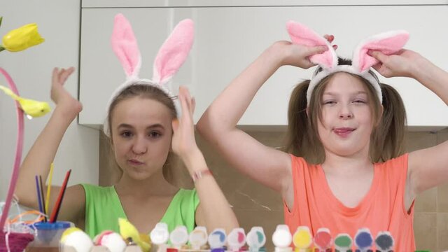 Two cute girls play with decorated Easter eggs and cover their eyes with their hands. Easter holiday. Rabbit ears on the head.