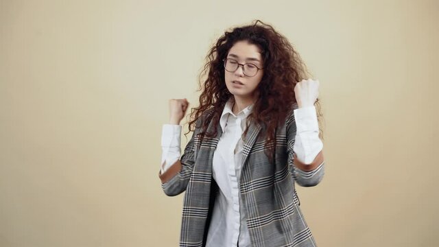The angry, angry young woman with her hands in her hair is shaking. Cretaceous in gray jacket and white shirt, with glasses posing isolated on a beige background in the studio. The concept of people's