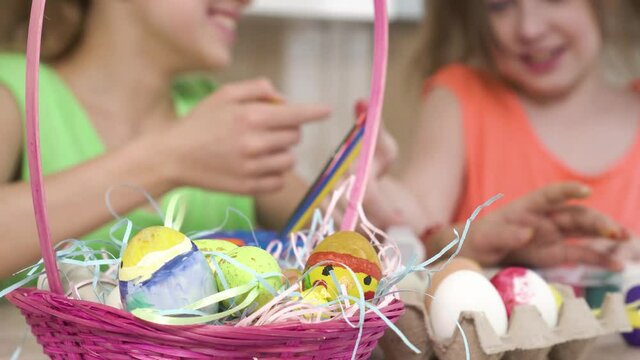 Beautiful pink wicker basket with Easter eggs. The girls play and paint on each other's faces. 4k video.