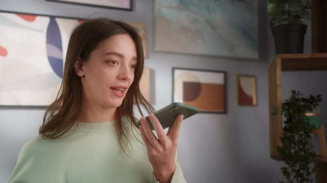 Happy young european woman talking and texting on smart phone, wearing casual clothes stay in room. Generation z students life, online shopping in campus, social media and audio conference.