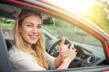 Happy beautiful woman is driving a red car.