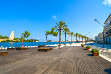 Palm trees line the waterfront boardwalk and promenade at the port harbor of Brindisi, Italy, in...