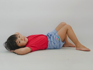 A portrait of smiling little girl, 4 years old, lying on the floor and looking at the camera, on a white blank background, copy space