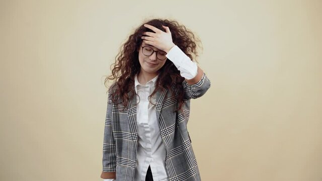 Ah rau The young woman who suffered a failure, depressed slaps her forehead. Cretaceous in gray jacket and white shirt, with glasses posing isolated on a beige background in the studio. The concept of