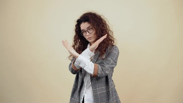 The responsible young woman, with folded hands, says stop, safety is at the forefront. Cretaceous in gray jacket and white shirt, with glasses posing isolated on a beige background in the studio. The