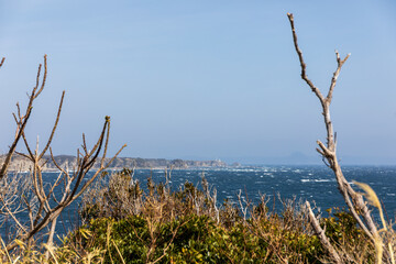 強風による白波に囲まれた岬の白い灯台を対岸から見る