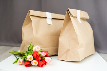 Kraft paper bags with blooming red tulips bouquet on gray background. flowers and food delivery...