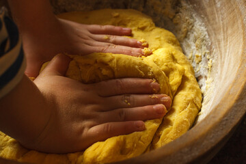 Children's hands knead the dough in a large wooden bowl for baking homemade bread, buns. Low key, selective focus, close up