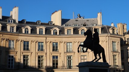Fototapeta premium Place des Victoires dans la ville de Paris, paysage urbain avec des immeubles haussmanniens et la silhouette de la statue équestre du roi soleil Louis XIV (France)