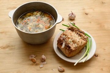 cauldron of soup and baked meat on a plate, green onion and garlic on wooden background, home cooking