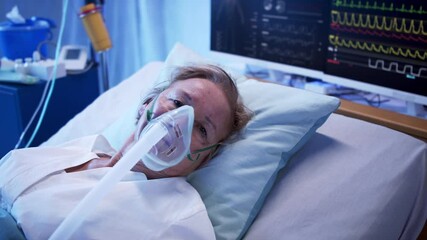 Covid-19 patient with oxygen mask in bed in hospital, looking at camera. Coronavirus concept.