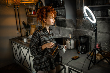 Female blogger with ring light and smartphone records video for social media in a kitchen. Blogger...