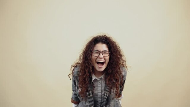 The desperate young woman cried out with a big mouth, leaning forward, fists down. Cretaceous in gray jacket and white shirt, with glasses posing isolated on a beige background in the studio. The